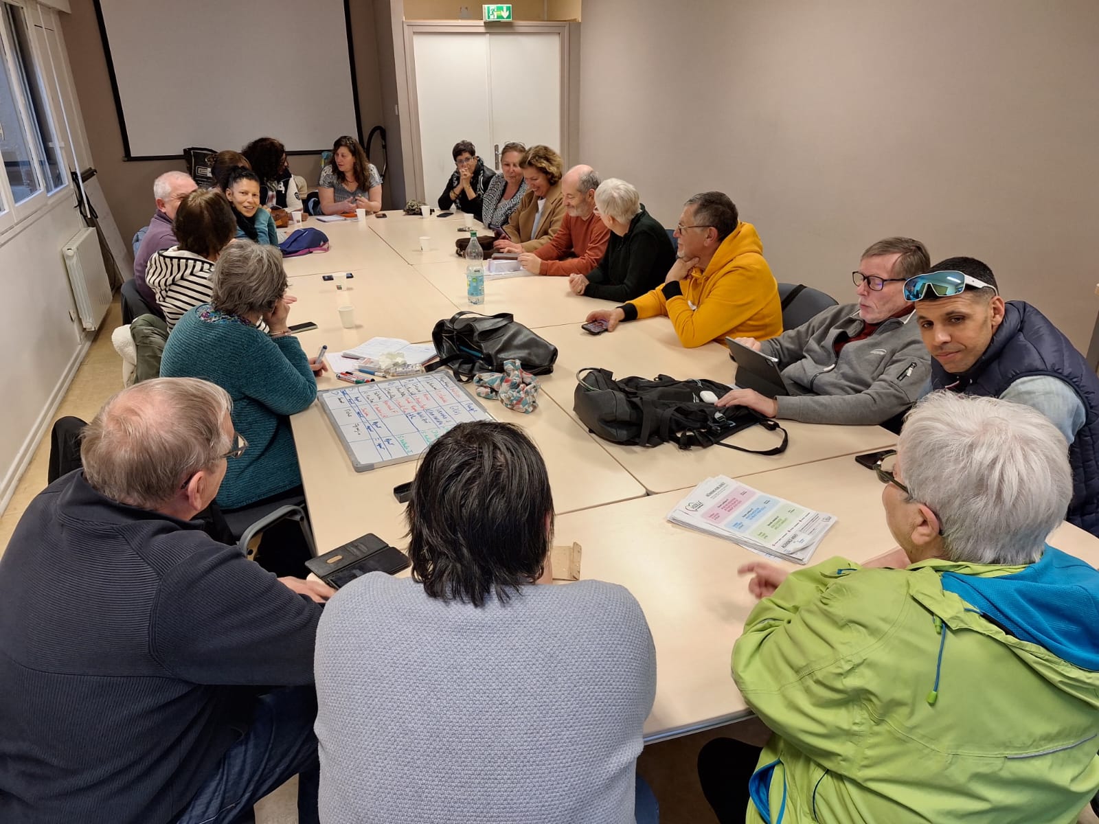 Réunion de travail interne — équipe au complet autour de la table, documents et tableau blanc