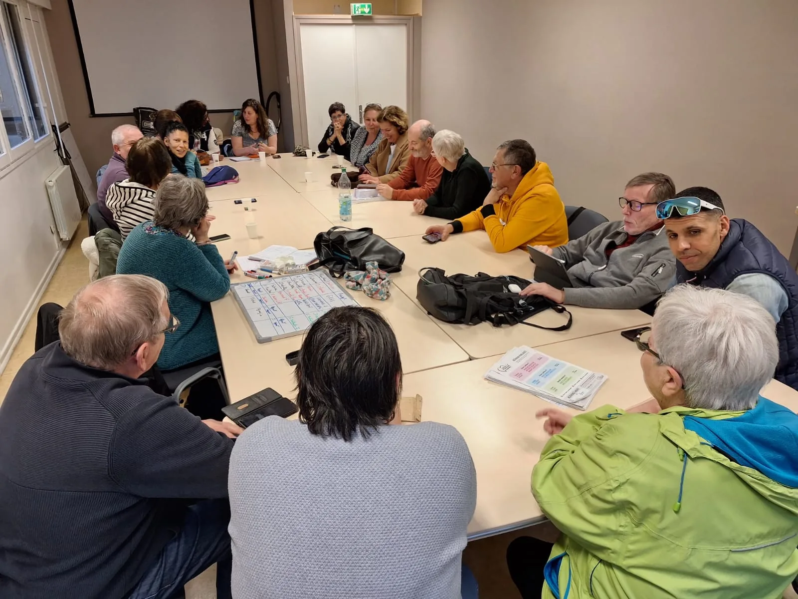 Réunion de travail interne — équipe au complet autour de la table, documents et tableau blanc